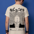 Man wearing beige Typocrisy SIL3NC3 oversized t-shirt, back graphic with SIL3NC3 musical notation title and illustrated silence figure, blue studio background
