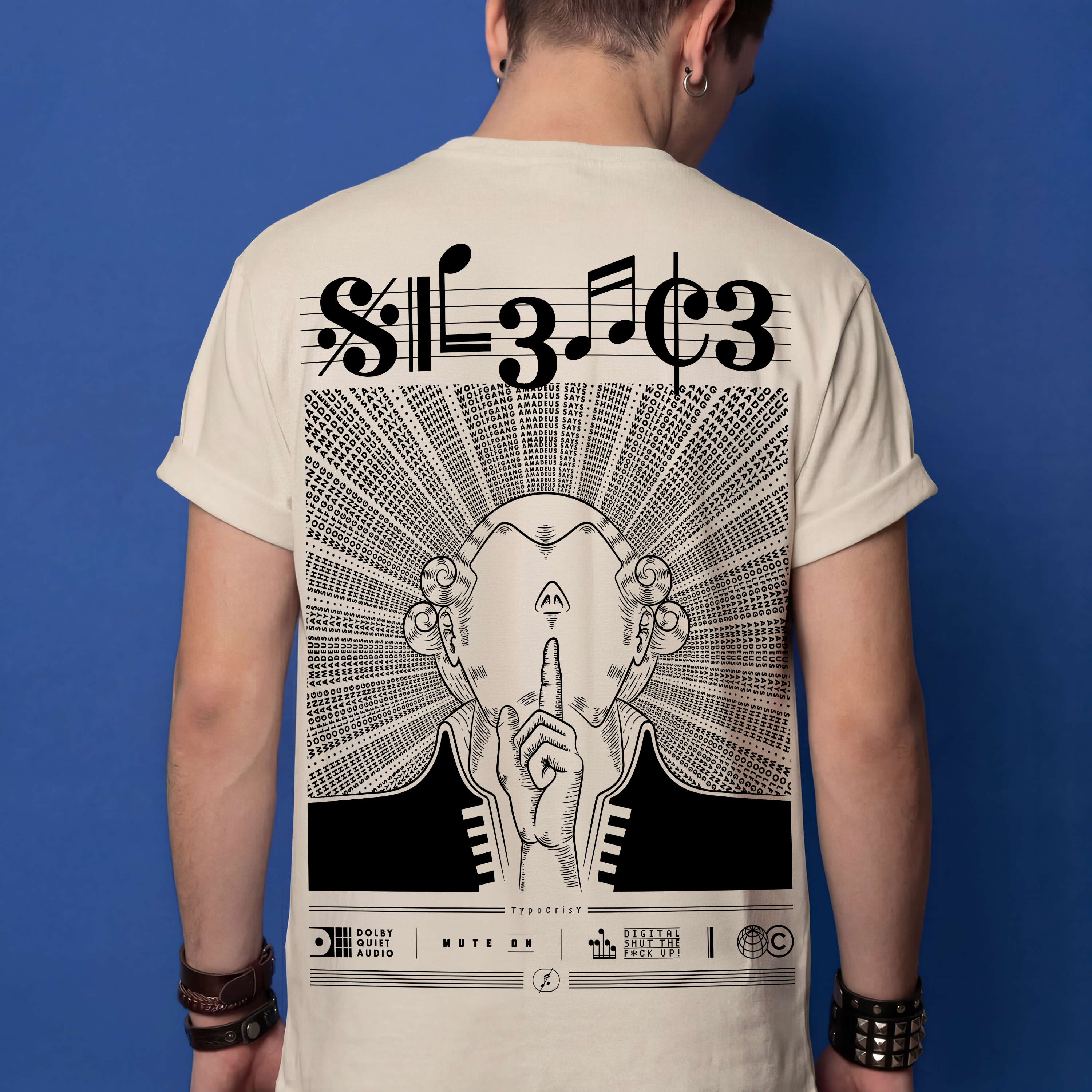 Man wearing beige Typocrisy SIL3NC3 oversized t-shirt, back graphic with SIL3NC3 musical notation title and illustrated silence figure, blue studio background