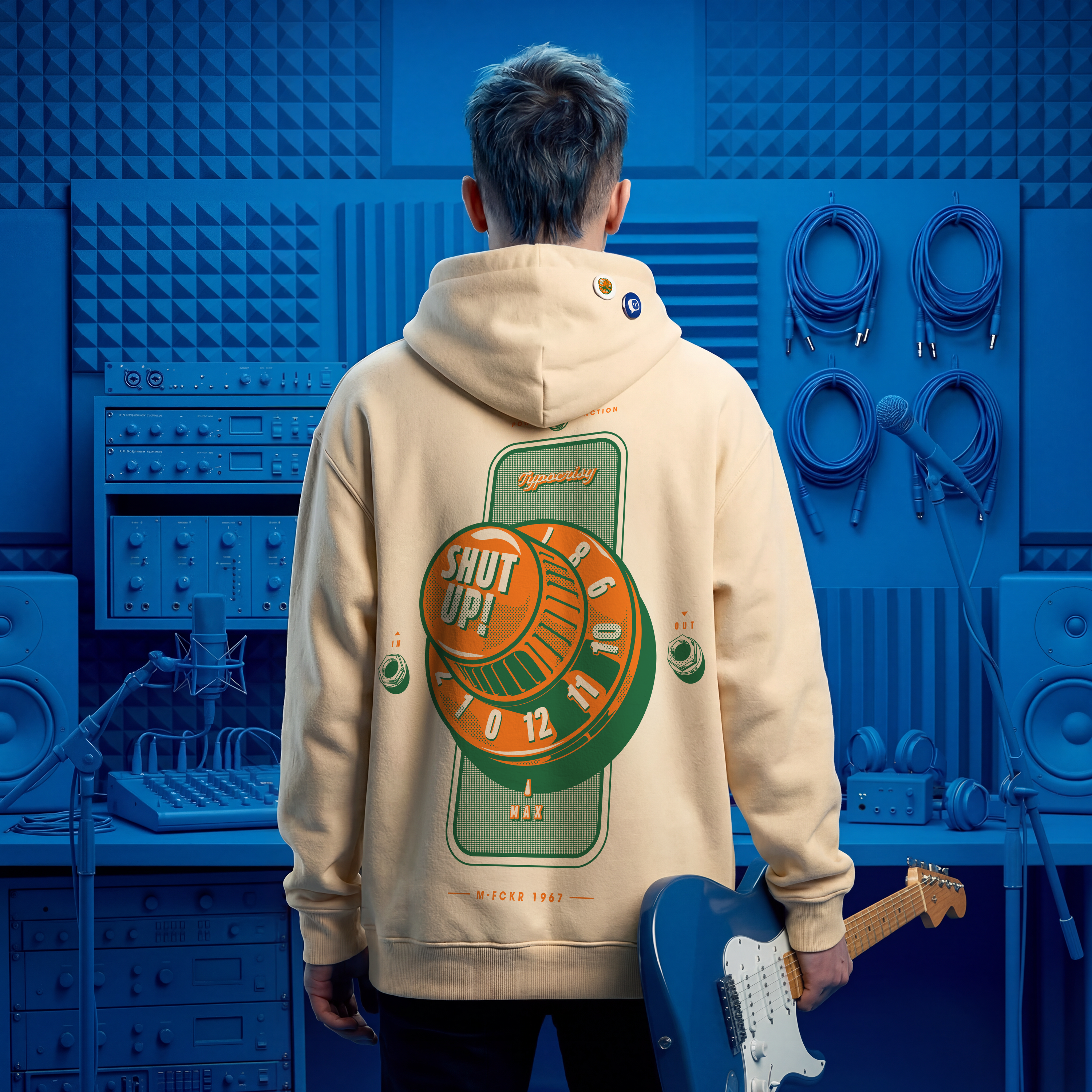 Person wearing a beige hoodie with a graphic design, holding a blue electric guitar in a blue-themed room.