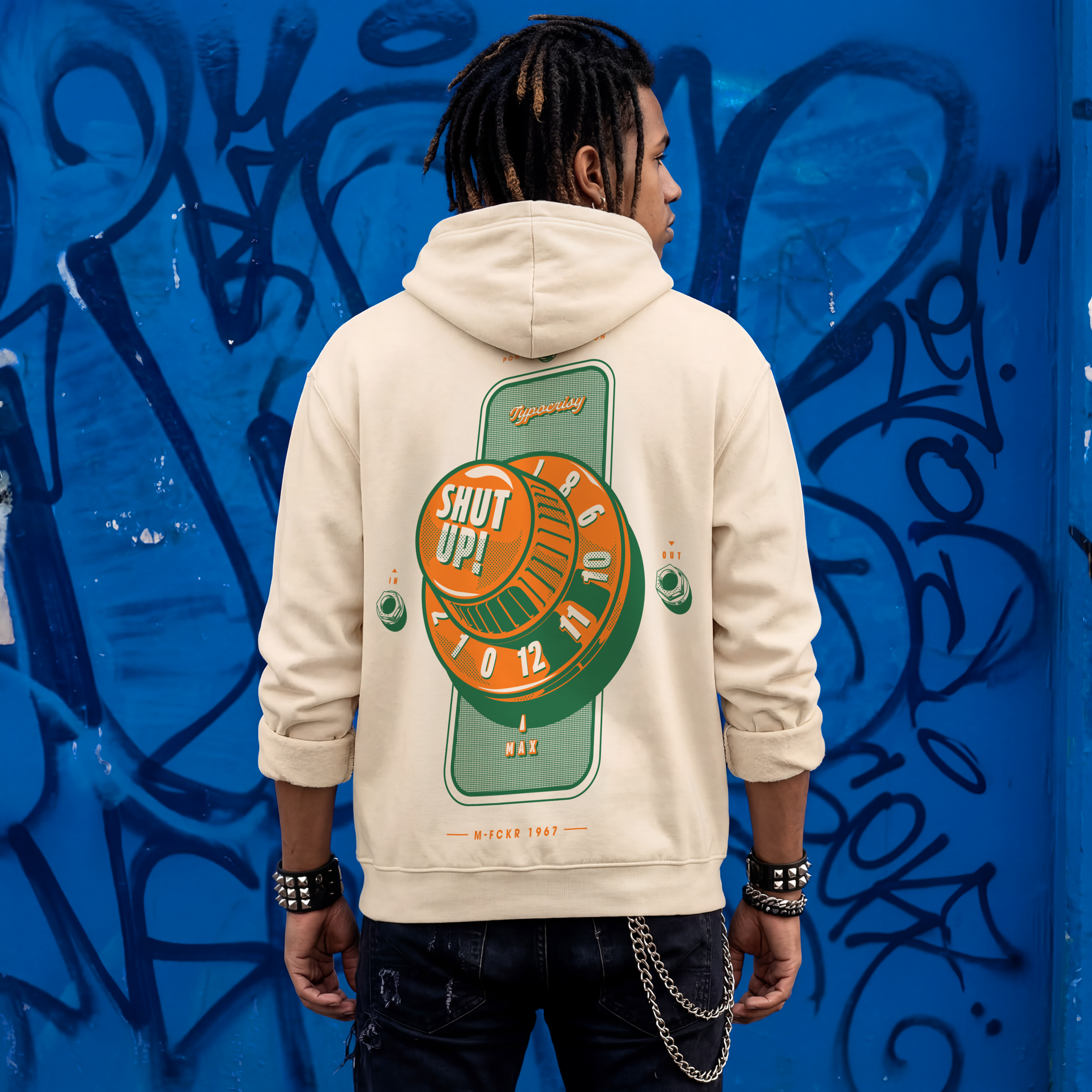 Person wearing a beige hoodie with a graphic design on the back against a blue graffiti-covered wall.