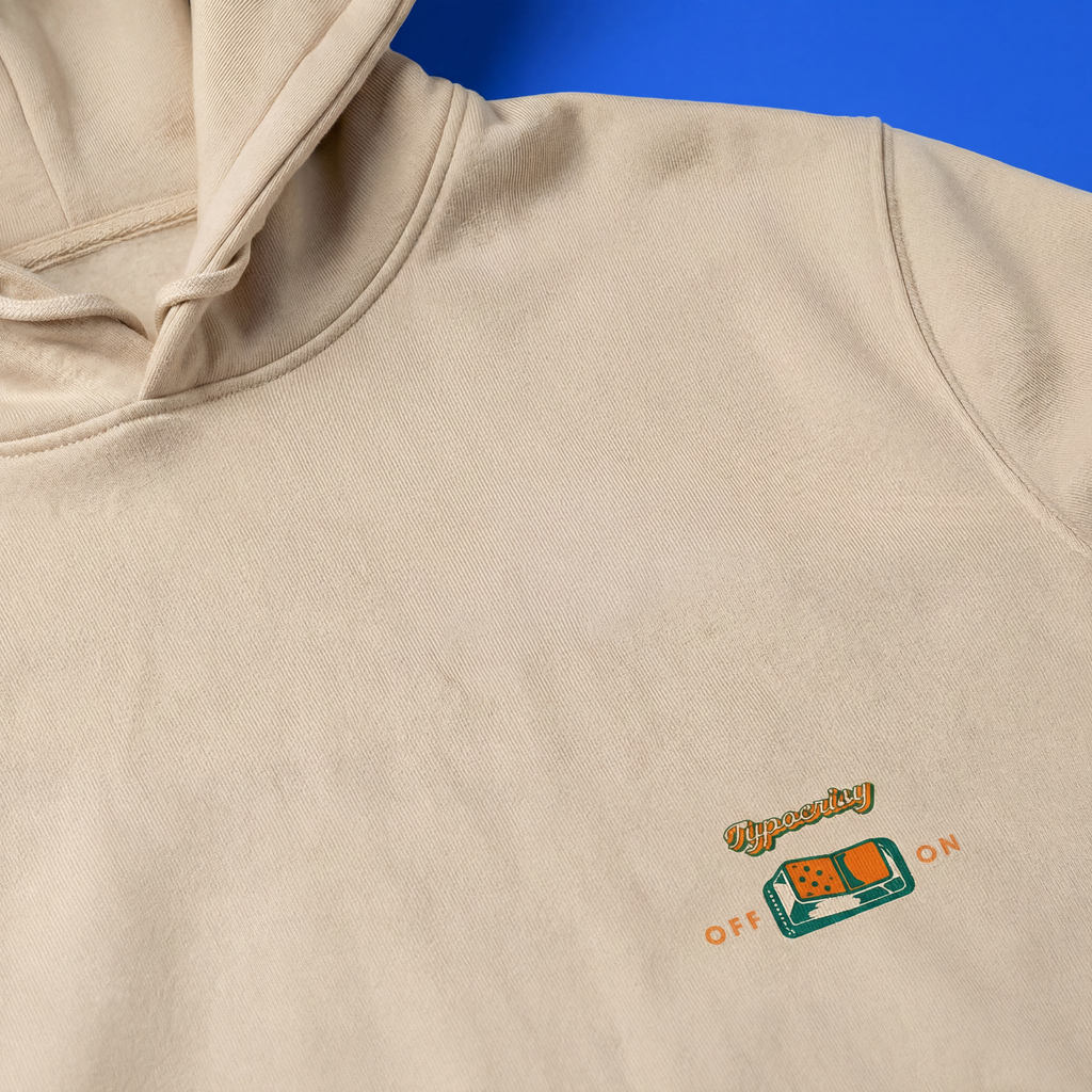 Beige hoodie with a small logo on the chest against a blue background