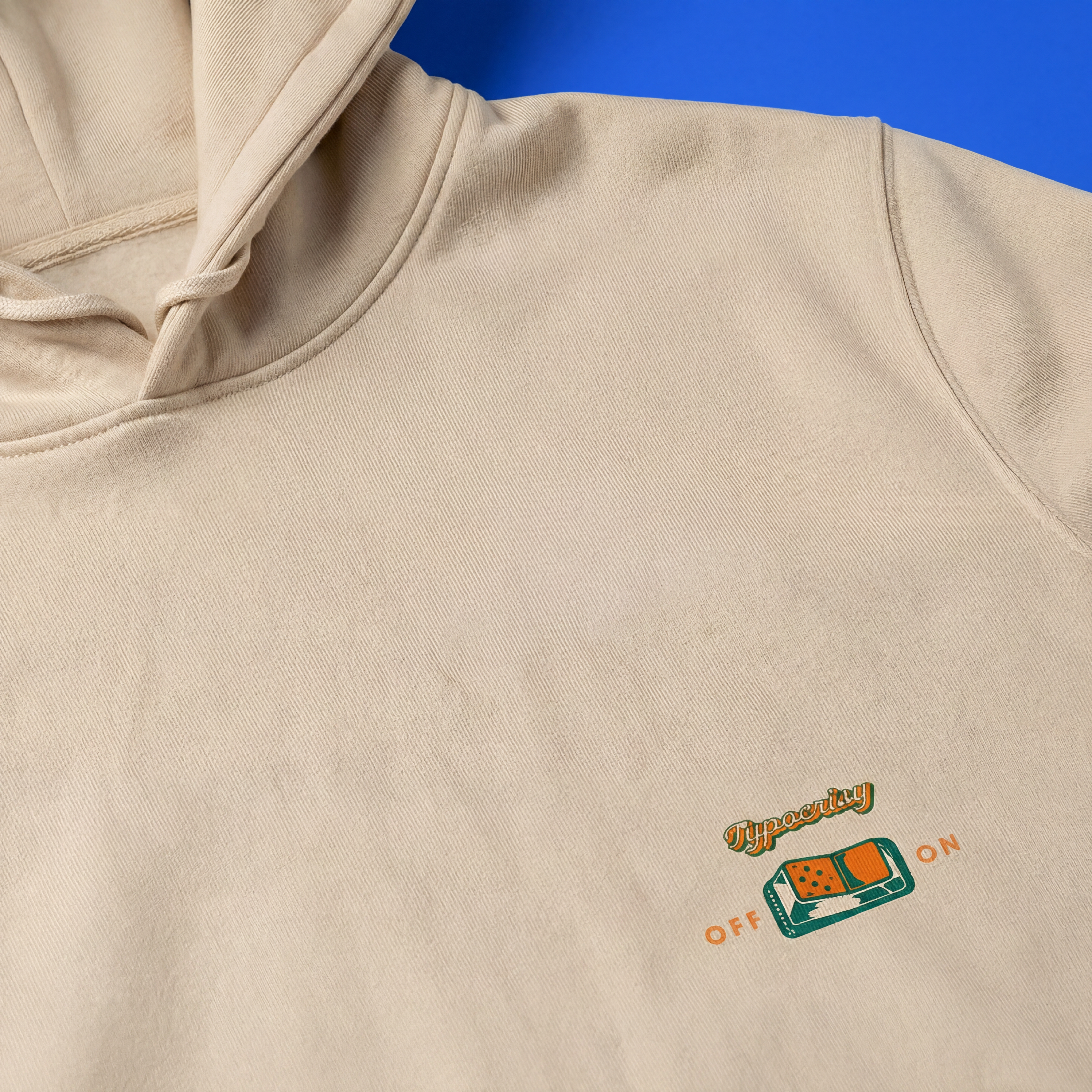 Beige hoodie with a small logo on the chest against a blue background