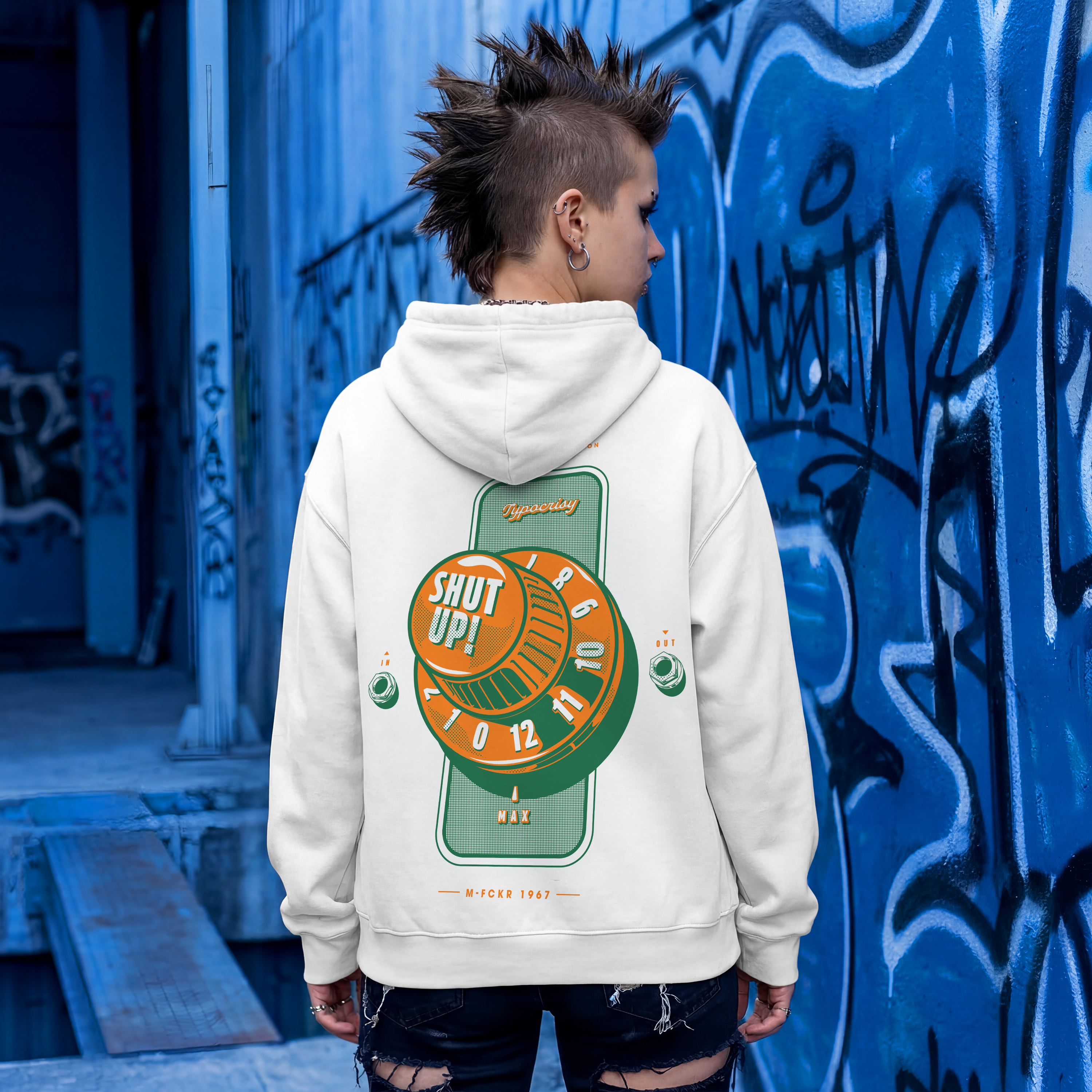 Person wearing a hoodie with a graphic design in front of a graffiti-covered wall.