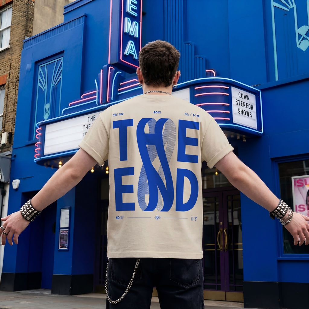 Person wearing a beige t-shirt with blue text in front of a blue building with neon signs.