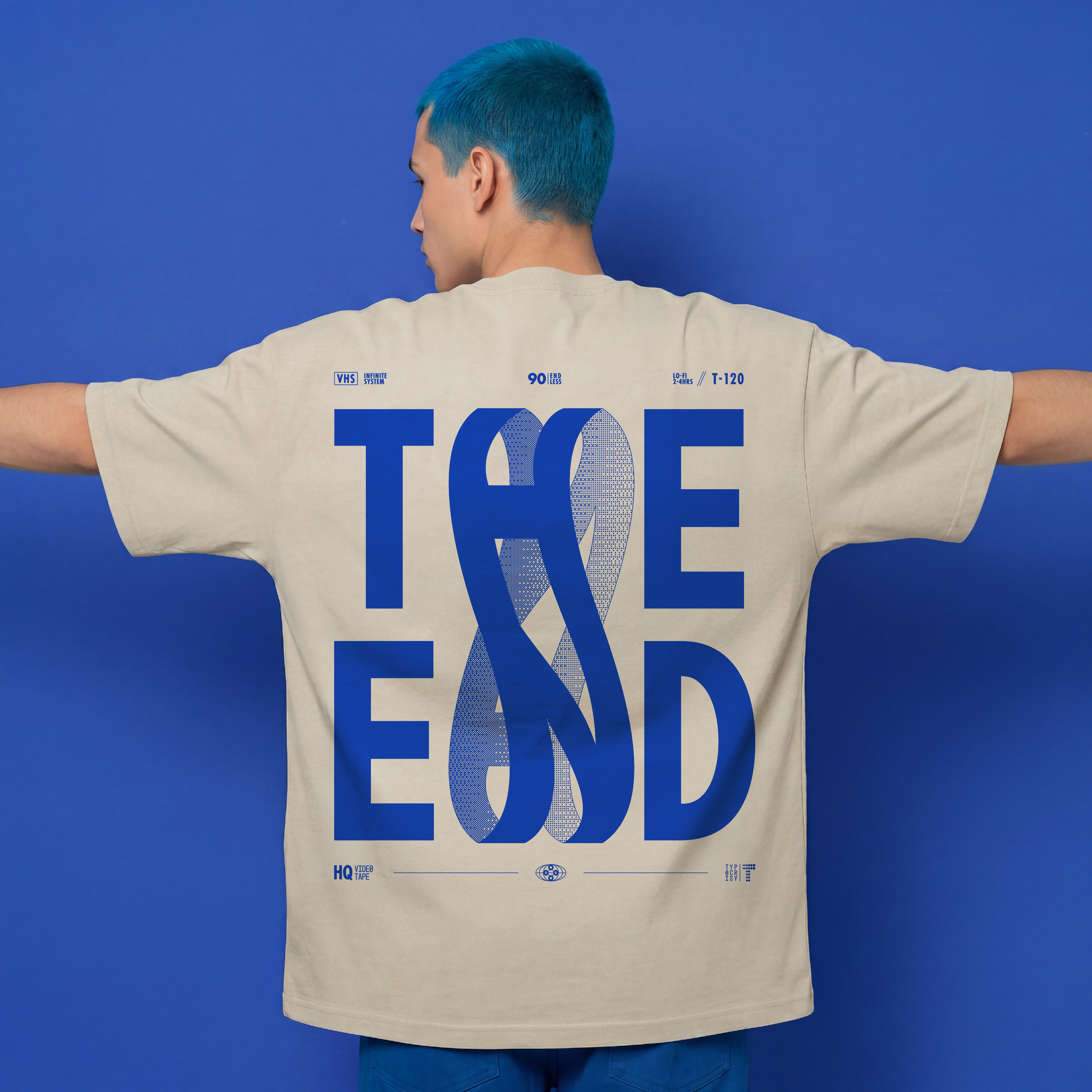 A person with bright blue hair stands with arms outstretched, wearing a cream-colored t-shirt with a large blue graphic print reading 'THE END' on the back, set against a solid blue background.