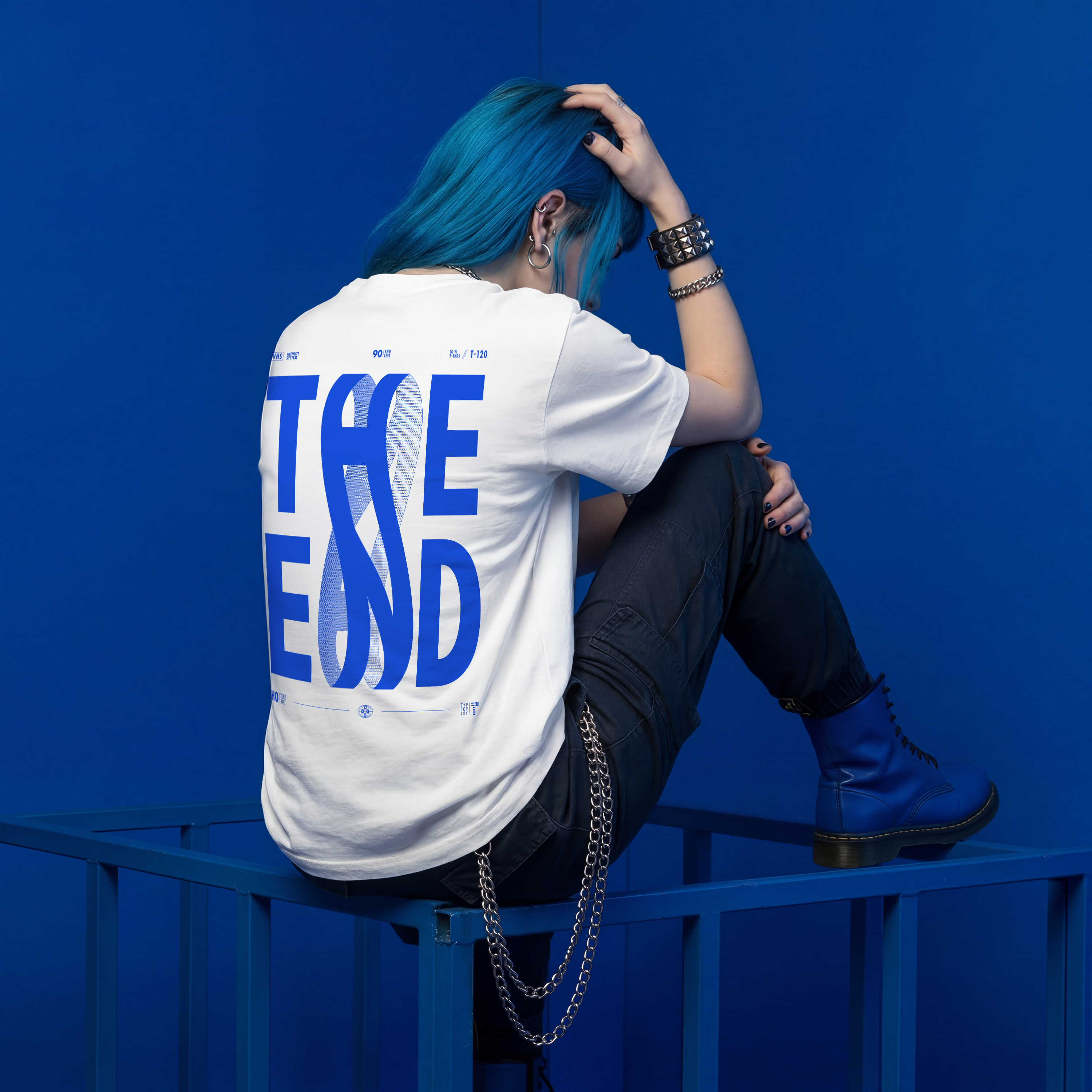 Person with blue hair sitting on a blue railing wearing a white t-shirt with blue text.