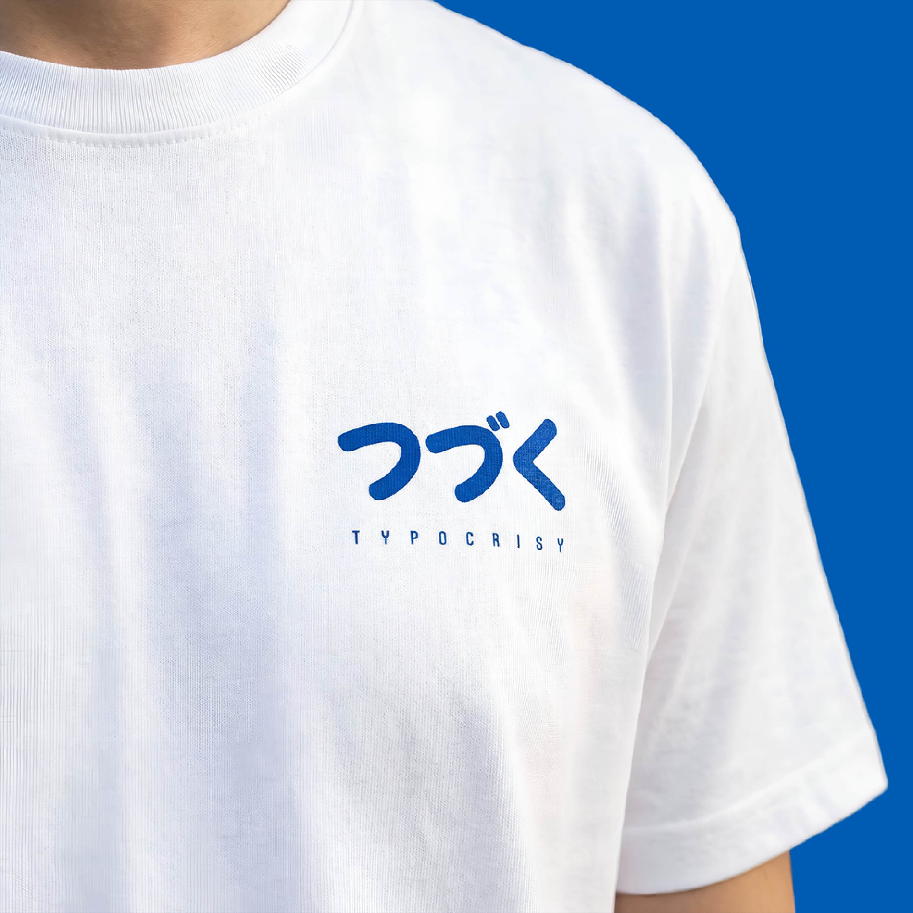 A close-up of a person wearing a white short-sleeve T-shirt with blue Japanese text and the word 'TYPOCRISY' printed on the chest, set against a solid blue background.