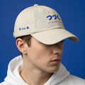 Person wearing a Typocrisy つづく To Be Continued Baseball beige cap with blue branding against a blue background