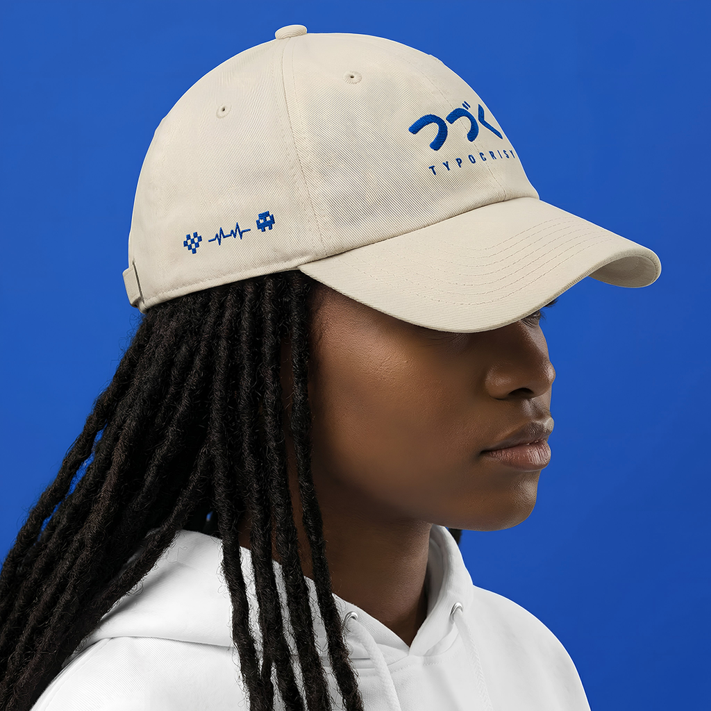 Person wearing a Typocrisy つづく To Be Continued Baseball beige cap with blue text on a blue background