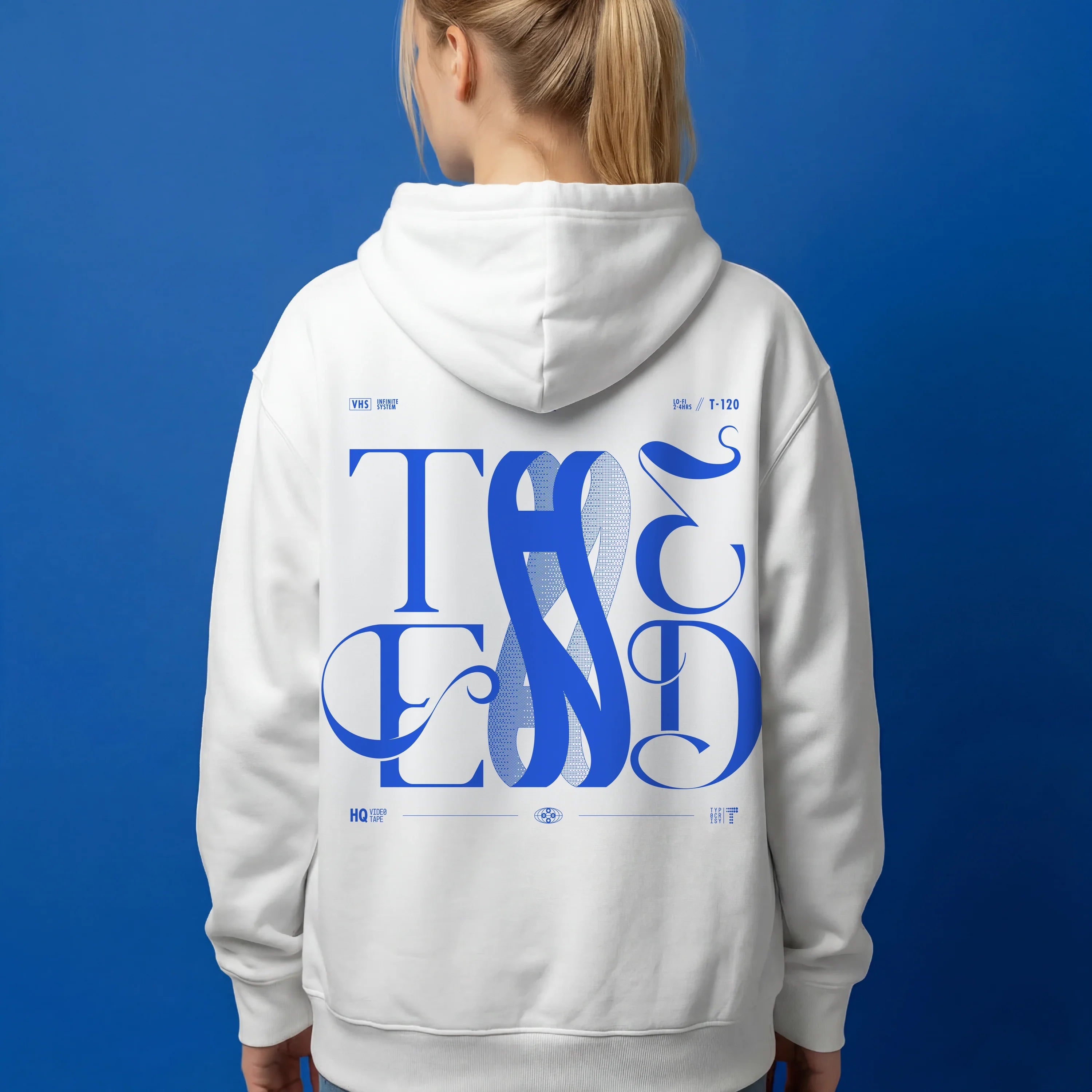 Back view of white oversized hoodie with large blue THE END interlocking baroque typography graphic, worn by a woman against a cobalt blue background — THE END Graphic Hoodie by TYPOCRISY