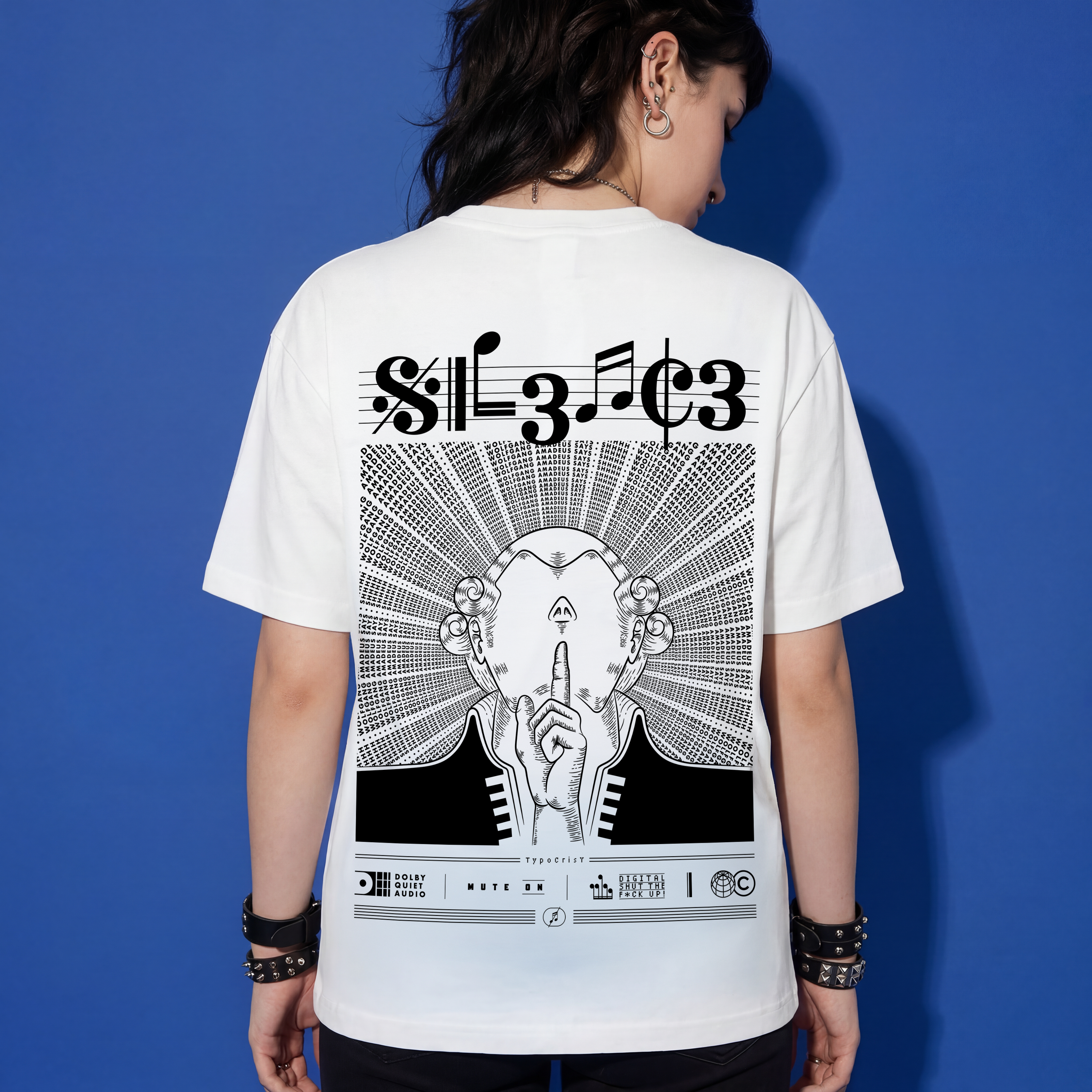 Woman wearing white Typocrisy SIL3NC3 oversized t-shirt, back graphic with SIL3NC3 musical notation title and illustrated silence figure, blue studio background