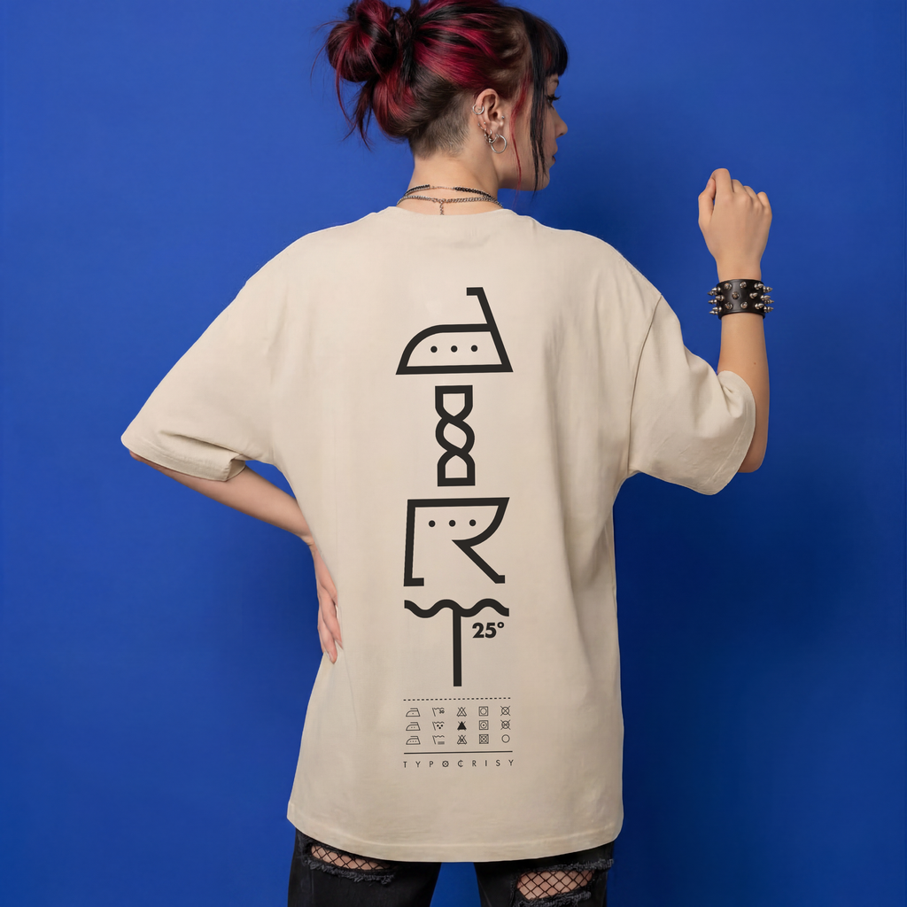Woman with red-tipped hair wearing beige Typocrisy DIRT 25 oversized t-shirt, back graphic spelling DIRT in laundry care symbols with 25° wash temp and TYPOCRISY wordmark, blue studio background